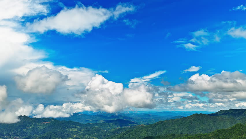 Aerial shot of the beautiful green mountain range and lush forest under a vast blue sky with fluffy clouds