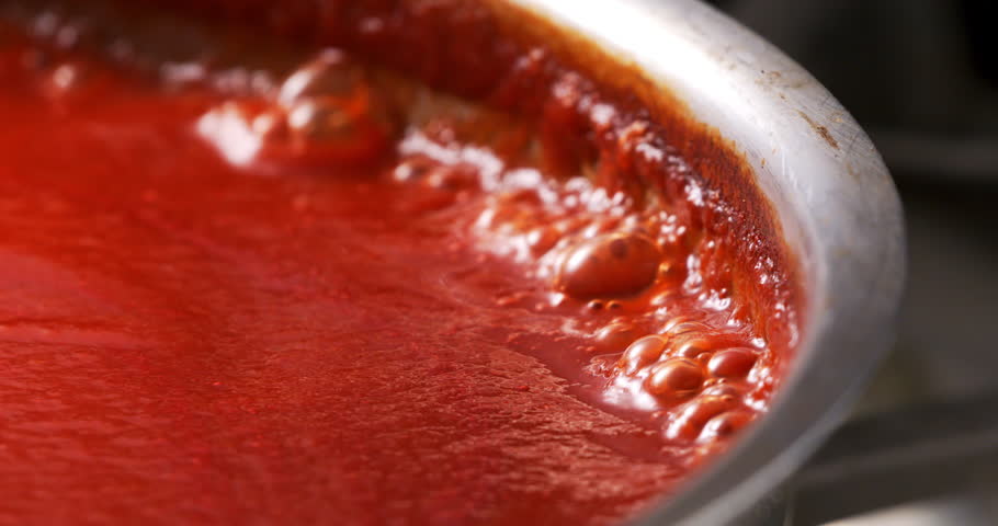 Slow motion close-up of homemade tomato sauce bubbling gently simmering in a metal pan under warm light at 1000 fps. Capturing the heart of Italian cooking tradition and culinary atmosphere.
