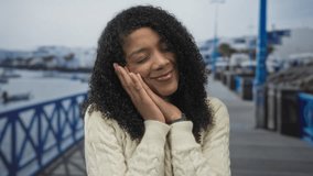 African american woman smiling gently holds hands to cheek on street by seaside promenade; serenity. - Powered by Shutterstock - Get 15% off with code: PIKWIZARD15