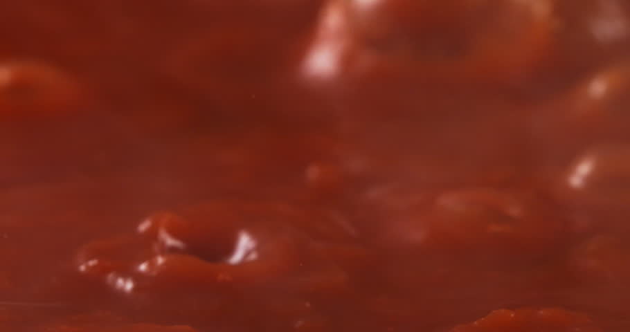 Slow motion macro of boiling rich red tomato sauce bubbling  naturally under warm light with deep red tones and soft steam at 1000fps. Concept of homemade Italian tradition and culinary passion.