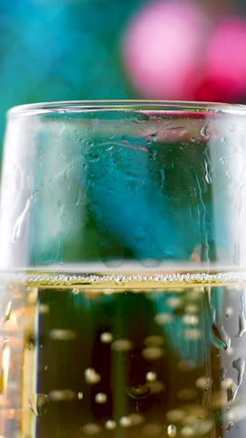 Champagne fills glasses, bubbles rise, adding sparkle. Soft candlelight and colorful bokeh create warm, festive mood. Christmas tree with decorations enhances joy. Leisure activity adds to celebration