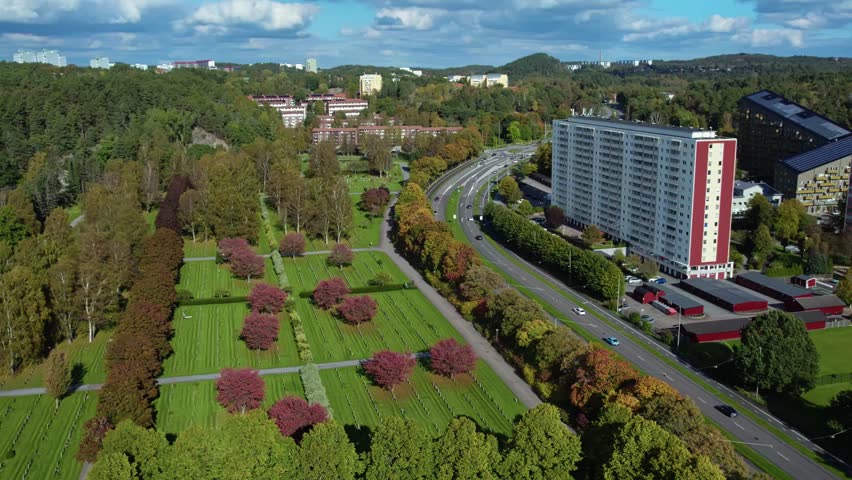 Kviberg Cemetery with aligned gravestones and red leaved trees bordered by forest and residential buildings in Gothenburg, Sweden.
