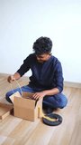 Young indian man unboxing lamp parts from open cardboard box on floor - Powered by Shutterstock - Get 15% off with code: PIKWIZARD15