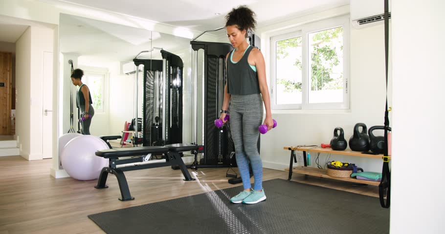 Young woman doing lunges with dumbbells in home gym, focused on exercise. fitness, workout, strength, training, wellness