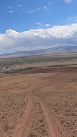 Vertical video of a car driving along a country road under blue sky. Altai desert and semi-desert environment. The village of Kokorya is visible in the valley.