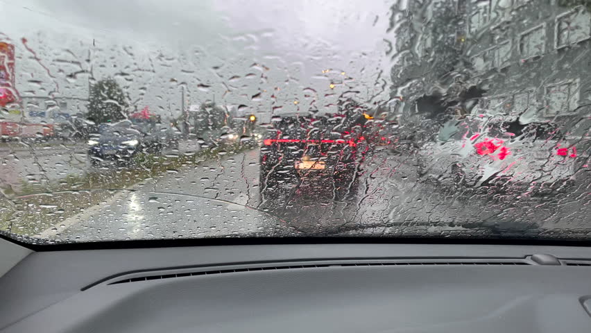 Driving in rainy weather seen from the inside of a car. Traffic on the rainy day at the city street from cabin seat through front window.