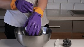 Woman cleaning a heavily soiled frying pan with a metal scrubber above a steel bowl in the kitchen, wearing protective gloves due to grease buildup - Powered by Shutterstock - Get 15% off with code: PIKWIZARD15