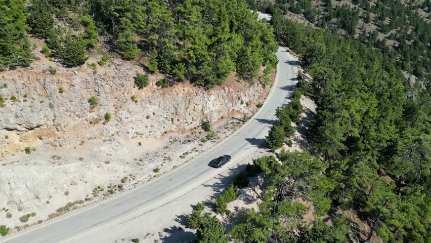 Adventure drive: drone footage of a single car traversing a remote mountain road through the woods. Evokes feelings of freedom, solitude and exploration on a long scenic journey