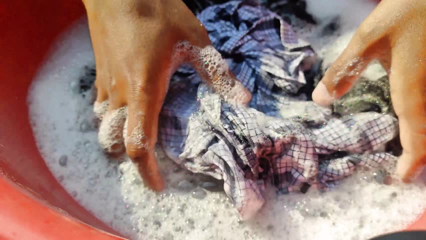 Clothes are being washed by hand with soap and water, creating foam and bubbles