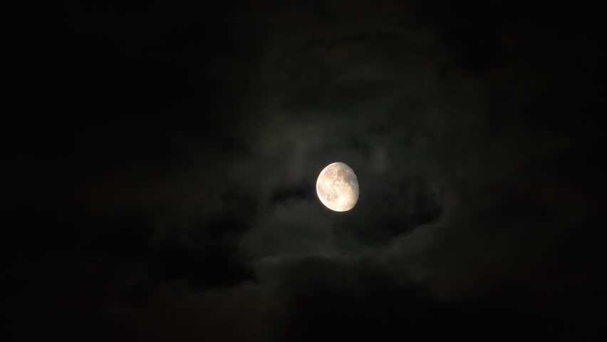 Mysterious waxing gibbous moon passing behind dark, dramatic clouds during a spooky night, creating a mystic and scary atmosphere perfect for Halloween and horror themes