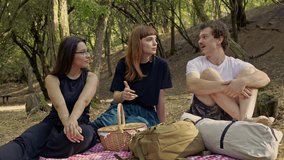 Three diverse friends enjoy a peaceful summer picnic in the forest, sharing conversations and laughter. This moment captures the essence of friendship, relaxation, and outdoor leisure activities. - Powered by Shutterstock - Get 15% off with code: PIKWIZARD15