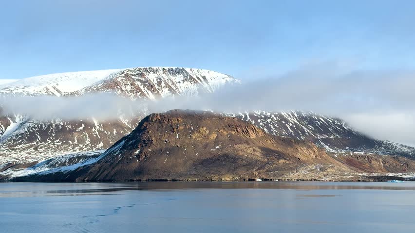 Majestic cliffs rise above tranquil waters in an arctic landscape under a bright sky