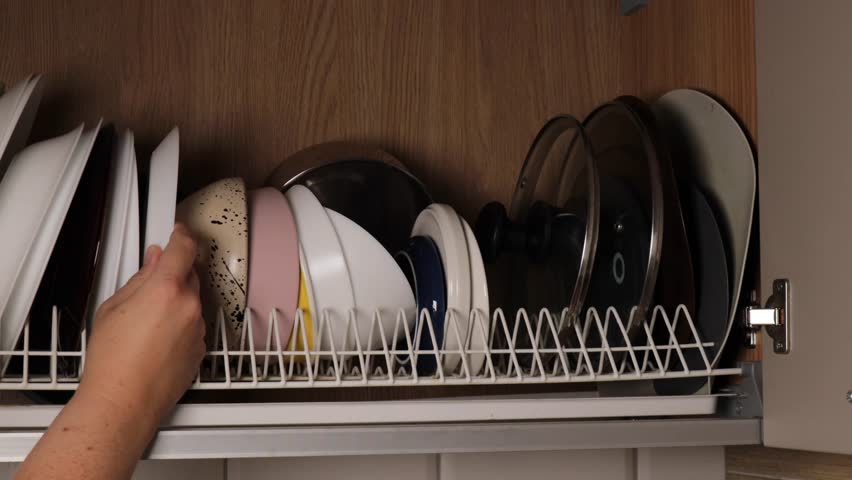 Hand placing clean plate carefully on kitchen shelf, plate arrangement symbolizing order, cleanliness, and comfort, ideal for household, lifestyle, or domestic routine footage.