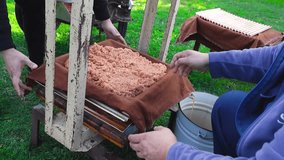 People making apple juice in a garden with a press by folding apple mush into small blankets and frames while apple juice is dripping from the press to a bucket on green grass in a garden, slow motion - Powered by Shutterstock - Get 15% off with code: PIKWIZARD15