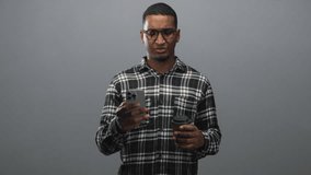 Black man wearing glasses and plaid shirt holding a smartphone in one hand and a takeaway coffee cup in the other, frowning while reading the screen in studio; confusion. - Powered by Shutterstock - Get 15% off with code: PIKWIZARD15