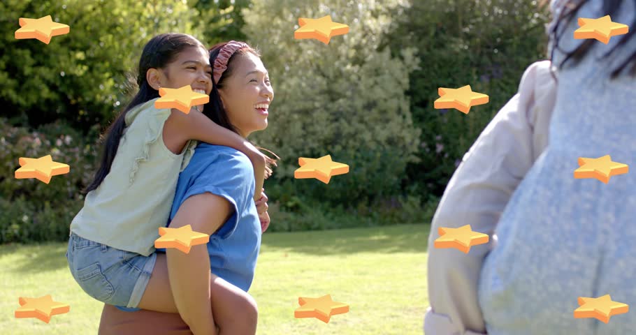 Woman piggybacking girl turning to greet nearby adult, orange stars passing in front in family park. Outdoor, playful, children, caregivers, lawn, sunshine, nature