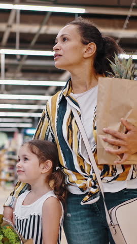 Portrait of lovely mom and daughter in supermarket with packages full of greens and fruits, healthy food, family shopping.