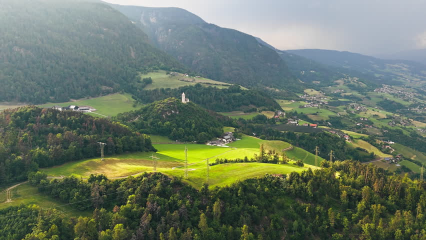 Open grasslands and agricultural plots around Chiesa di Santa Verena in low sun, aerial view. Northern Italy rural environment in evening light