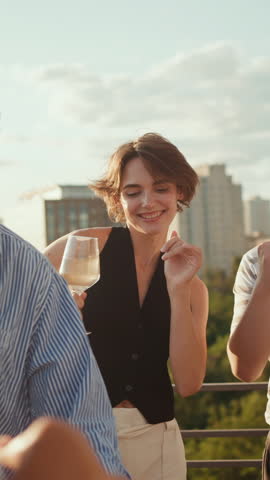International young people dressed in casual wear enjoying beat of driving music during rooftop party at big city. Lively men and women drinking alcohol, chatting and relaxing together among weekends.