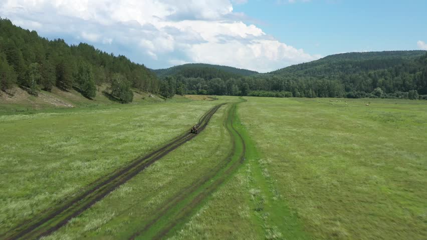 Farmer driving small tractor along a dirt road, surrounded by lush green fields under a bright blue sky