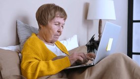Mature senior woman with a focused expression working from home, typing on a laptop computer while comfortably sitting in bed, staying connected through modern wireless technology - Powered by Shutterstock - Get 15% off with code: PIKWIZARD15