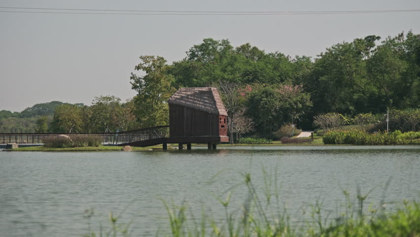 A Cinematic Wide-Angle Landscape of a Wetland Park, Featuring Rippling Lake Water, Green Grassland, Distant Mountains, and Blue Sky (ProRes 422)