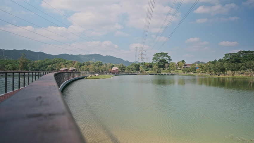 A Cinematic Wide-Angle Landscape of a Wetland Park, Featuring Rippling Lake Water, Green Grassland, Distant Mountains, and Blue Sky (ProRes 422)