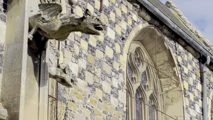 Gothic gargoyles and flint-limestone checkerboard wall of Saint-Martin Church, Saint-Valery-sur-Somme, Picardy, with ornate tracery, lancet windows and slate roof details under a bright autumn sky