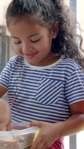 Vertical video: Child girl grabbing sandwich halves from container at patio and biting it to eat. Youth, snack, outdoor, relaxed, candid, natural, vertical video