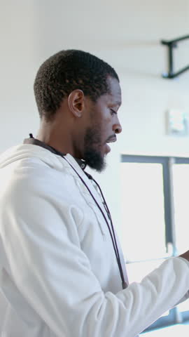 Vertical video: African American male coach scanning tablet at gym on cue, turning, calling player. Athlete, mentorship, determination, athleticwear, fitness, teamwork, vertical video
