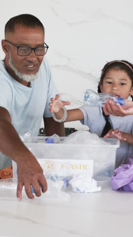 Diverse father and child sorting plastic recyclables at counter, with PLASTIC bin and orange bag. Sustainability, environmental, education, domestic, eco-friendly, community, engagement