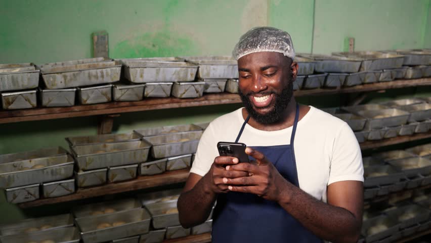 Local African baker, successful small business entrepreneur uses his smartphone for client video calls, online orders, digital banking and social media in his bakery, SME