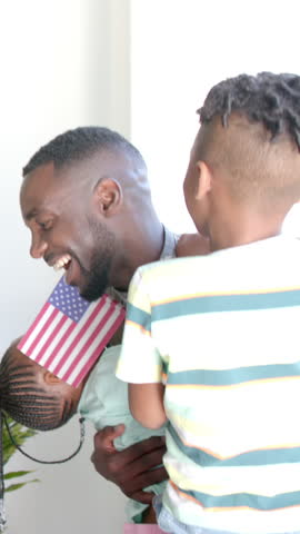 African American father and son standing in room by window, with camo uniform and striped shirt. Fatherhood, childhood, protection, bond, family, resilience, masculinity