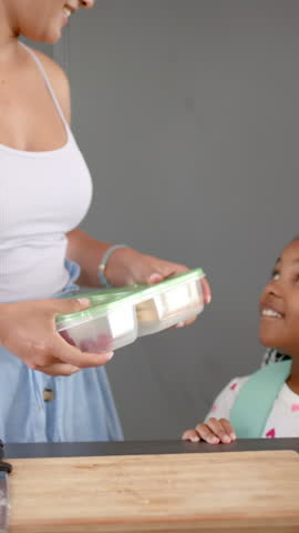 Vertical video: Mother and daughter placing lunch box on kitchen counter after spotting hunger cue. Family, nurturing, domestic, caregiving, cheerful, cozy, vertical video