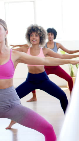 Vertical video: Female instructor entering gym guiding two female students lunging into warrior II. Wellness, flexibility, strength, body alignment, ensemble, movement, vertical video