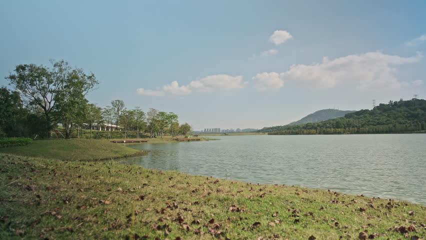 A Cinematic Wide-Angle Landscape of a Wetland Park, Featuring Rippling Lake Water, Green Grassland, Distant Mountains, and Blue Sky (ProRes 422)