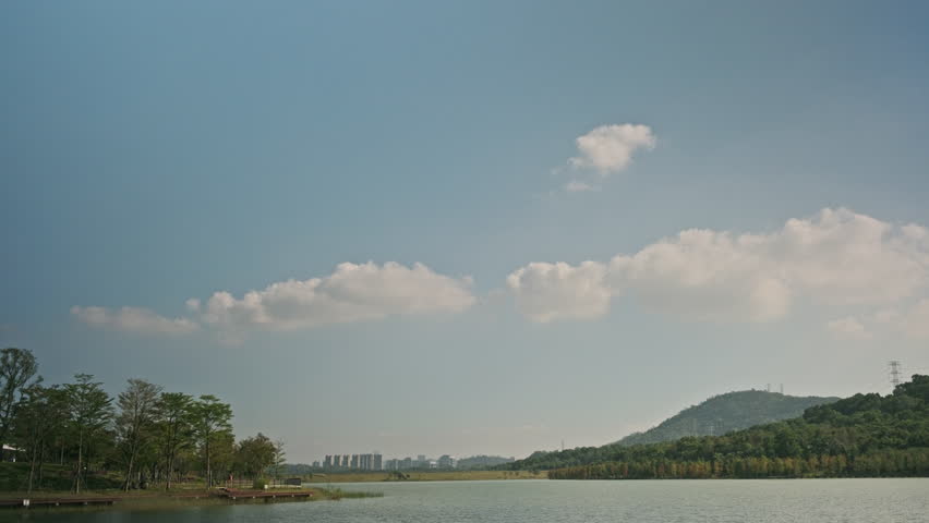 A Cinematic Wide-Angle Landscape of a Wetland Park, Featuring Rippling Lake Water, Green Grassland, Distant Mountains, and Blue Sky (ProRes 422)