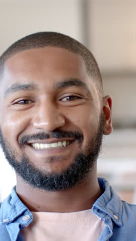 Vertical video: African American man smiling at home, grinning and laughing in softly lit room. Portrait, happiness, warmth, candid, lifestyle, cozy, vertical video