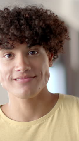 Vertical video: Man reacting to camera, shifting from neutral gaze to broad laughter in bright room. Joy, spontaneity, expression, positivity, warmth, candid, vertical video