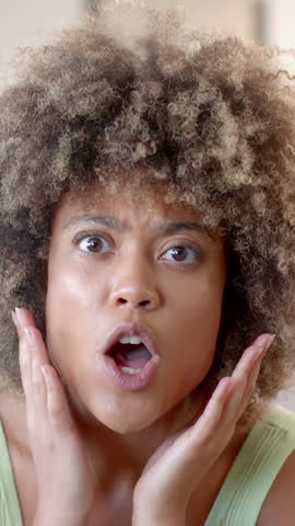 Vertical video: Reacting to surprise, African American woman pleading and laughing for fun at home. Expressive, candid, joyful, natural, vibrant, approachable, vertical video