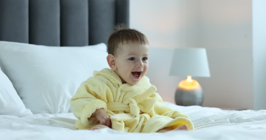 Cute baby in bathrobe on bed at home
