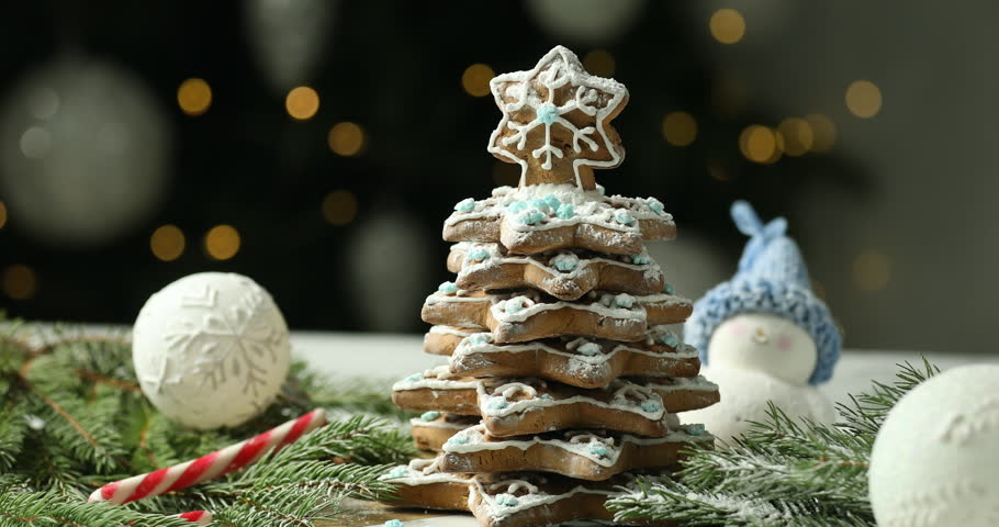 Sprinkling powdered sugar onto delicious Christmas cookie tree with icing and decor on white table against grey background with blurred lights, closeup