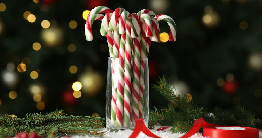 Many candy canes in glass on artificial snow against blurred background with twinkling Christmas lights. Bokeh effect