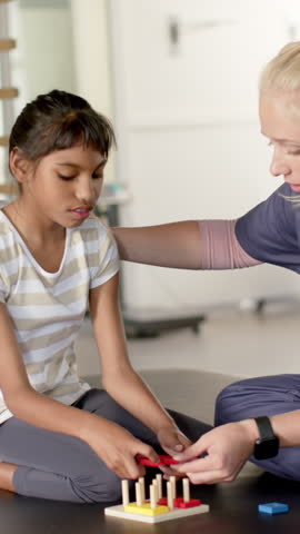 Vertical video: Therapist placing ring and guiding Asian girl stacking rings on pegboard on mat. Child development, occupational therapy, sensory play, pediatric therapy, fine motor skills,