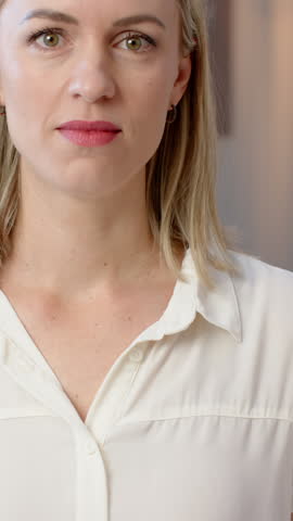 Vertical video: Mid-adult woman wearing blouse turning from calm to laugh at home as camera zooming. Emotion, authenticity, warmth, serenity, candid, personal, vertical video