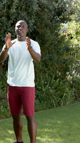 African American man holding American football and aiming toss in backyard, with green shrubs. Sports, leisure, outdoor, activity, casual, vibrant, fitness