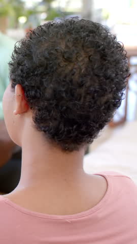 Vertical video: Woman hearing her name called turning head at dining table in pink top smiling. Lifestyle, connection, candid, warm, casual, joyful, vertical video