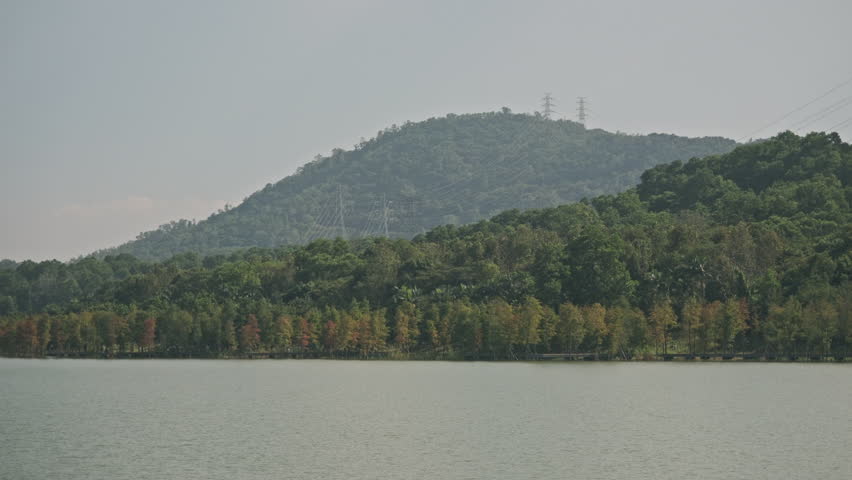 A Cinematic Wide-Angle Landscape of a Wetland Park, Featuring Rippling Lake Water, Green Grassland, Distant Mountains, and Blue Sky (ProRes 422)