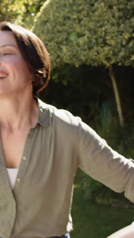 Vertical video: Diverse family stepping into warm hug after mother opening arms in sunlit backyard. Family, kinship, affection, outdoor, lifestyle, warm, vertical video