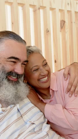 Laughing senior couple embracing indoors against wooden panel backdrop, sharing joyful moment. Romance, companionship, serenity, affection, warmth, vitality, connection